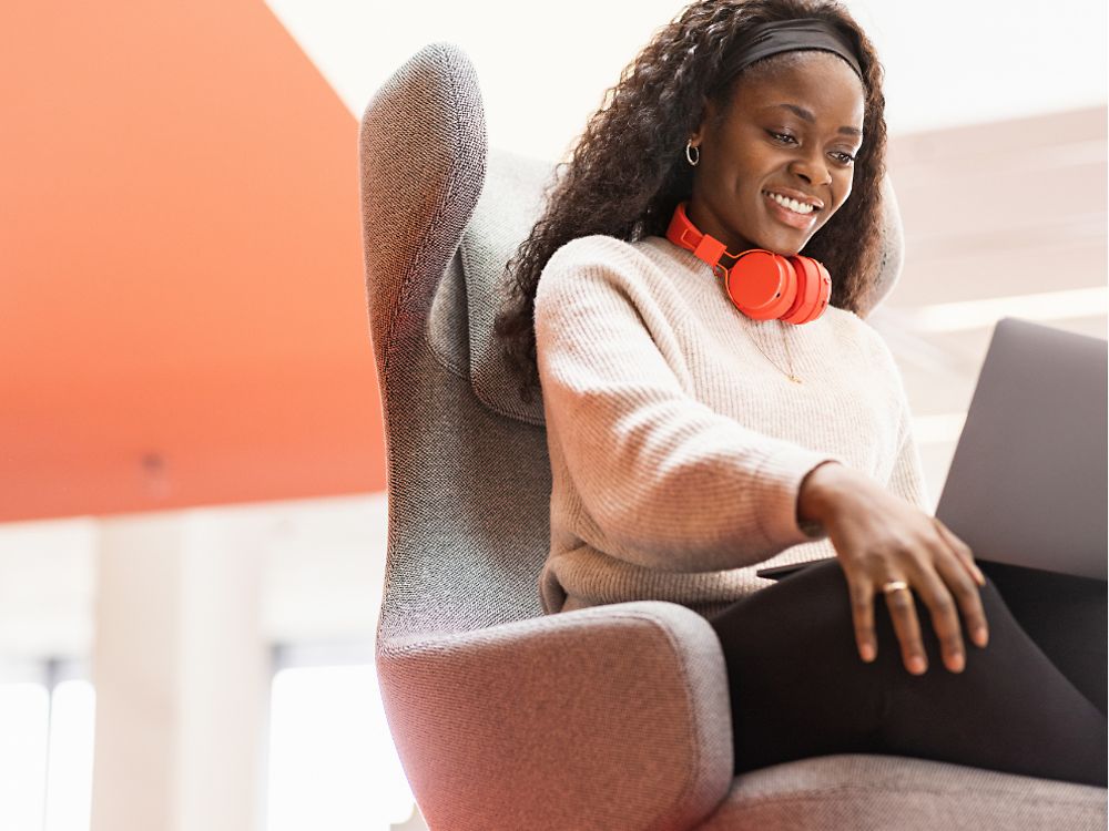 O angajată Henkel stă pe un scaun confortabil cu laptopul în genunchi. Ea zambeste. 