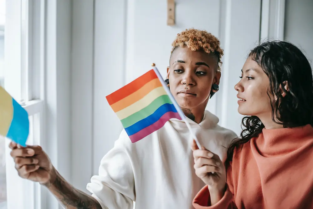 Două femei vorbesc între ele în timp ce țin un steag LGBTQ+.