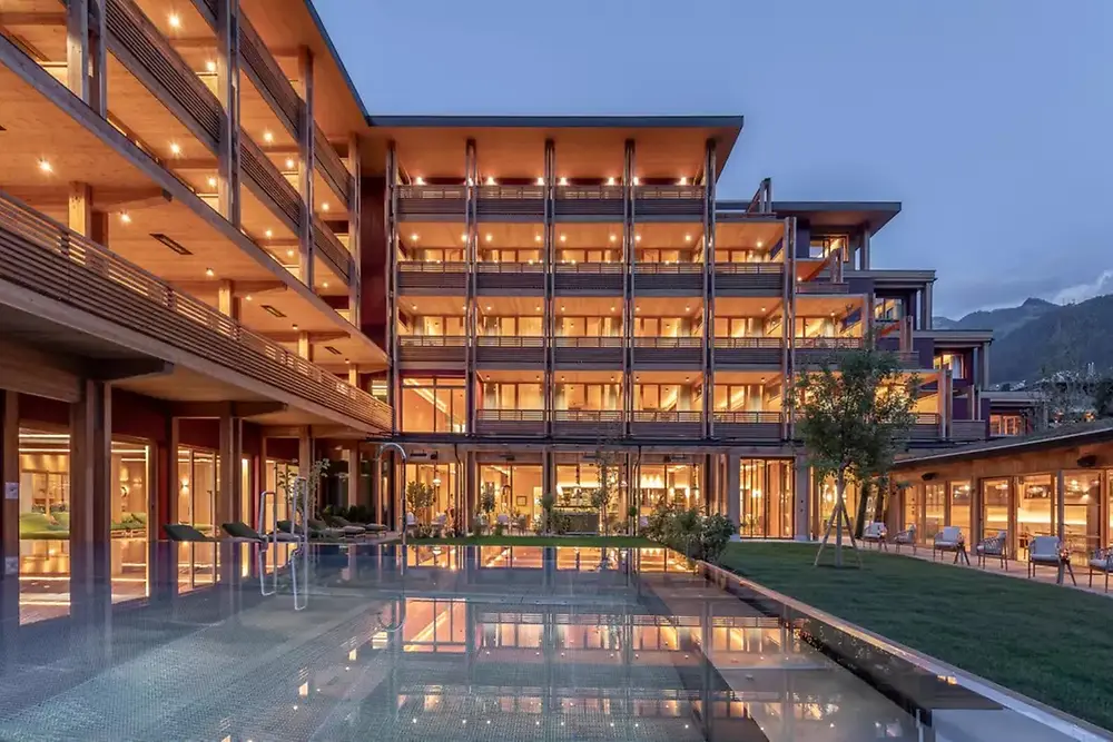 Clădire comercială modernă, cu exterior iluminat și piscină reflectorizantă la amurg.