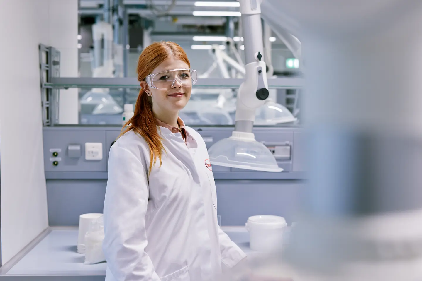 Absolvent care își începe cariera la Henkel, purtând un halat alb de laborator și stând într-un mediu modern de laborator, cu echipamente tehnice în fundal.