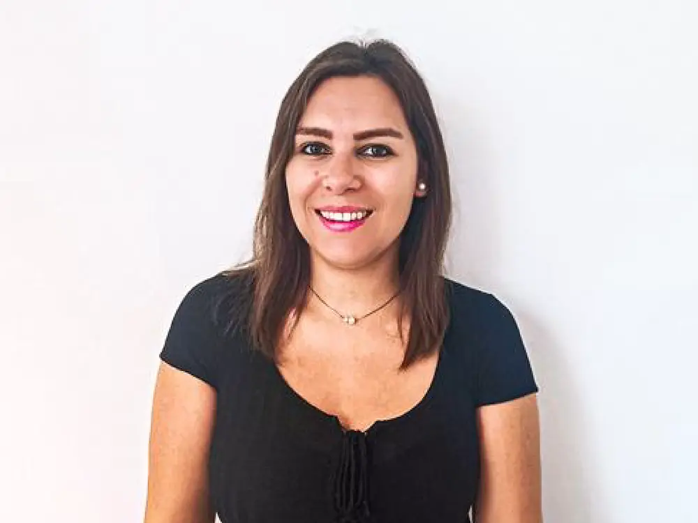 Un partener de recrutare stând în picioare în fața unui fundal alb, purtând un top negru și o centură bej, împărtășind sfaturi despre cum să gestionați întrebările dificile din cadrul interviului.