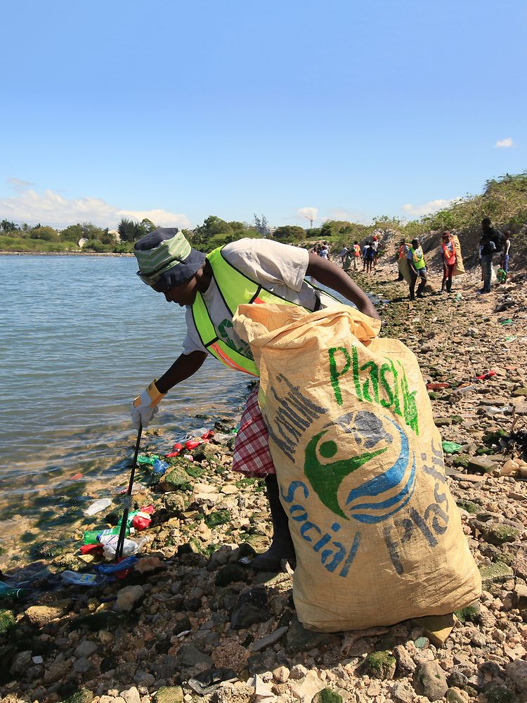 Femeie care colectează deșeuri din plastic de pe plajă